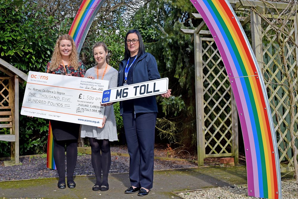 M6toll employee holding M6toll sign poses next to two ladies from Acorns Hospice with giant cheque